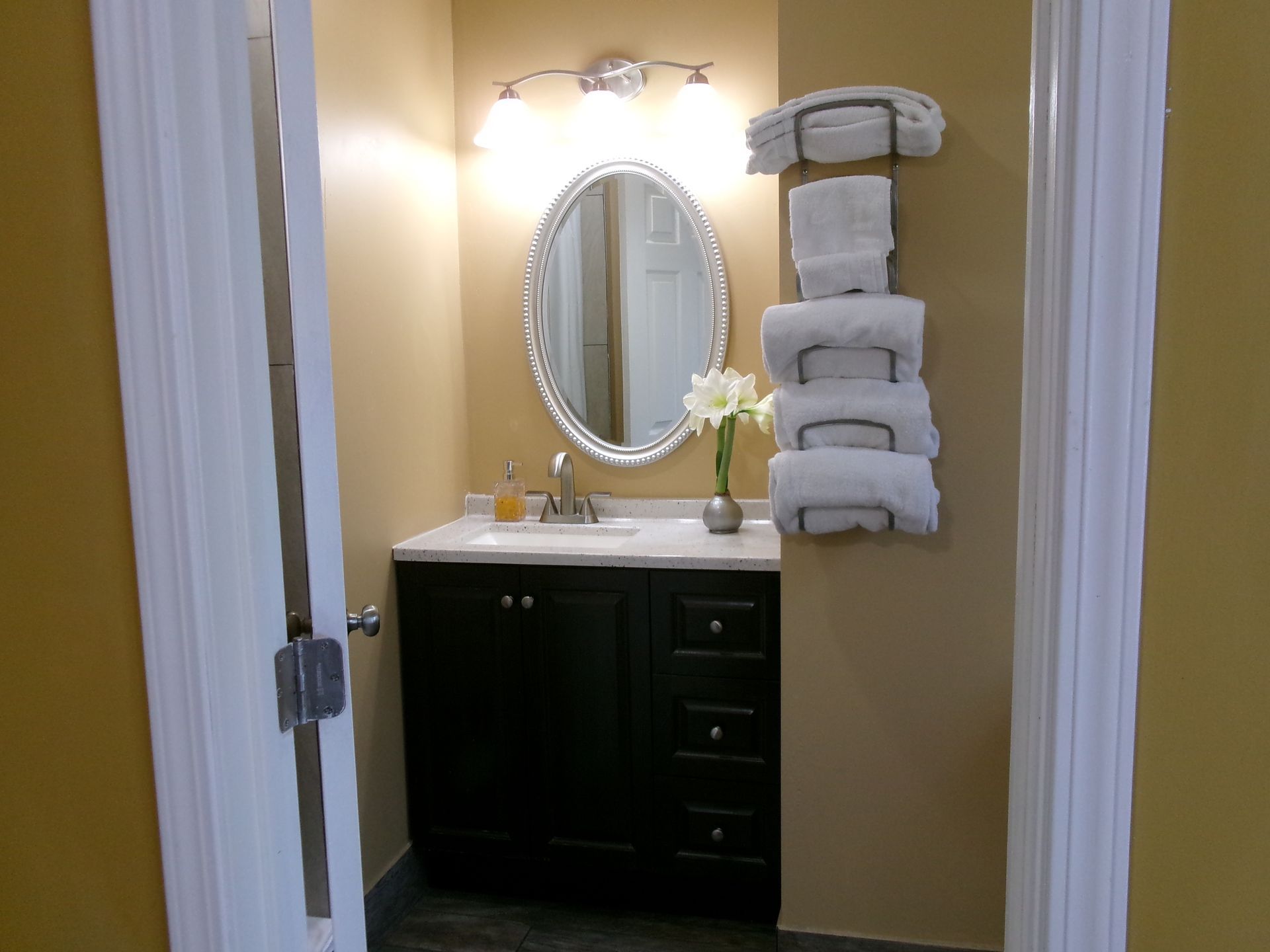 A bathroom vanity featuring a dark wood cabinet, oval mirror, wall-mounted light, and a stack of towels on the wall.