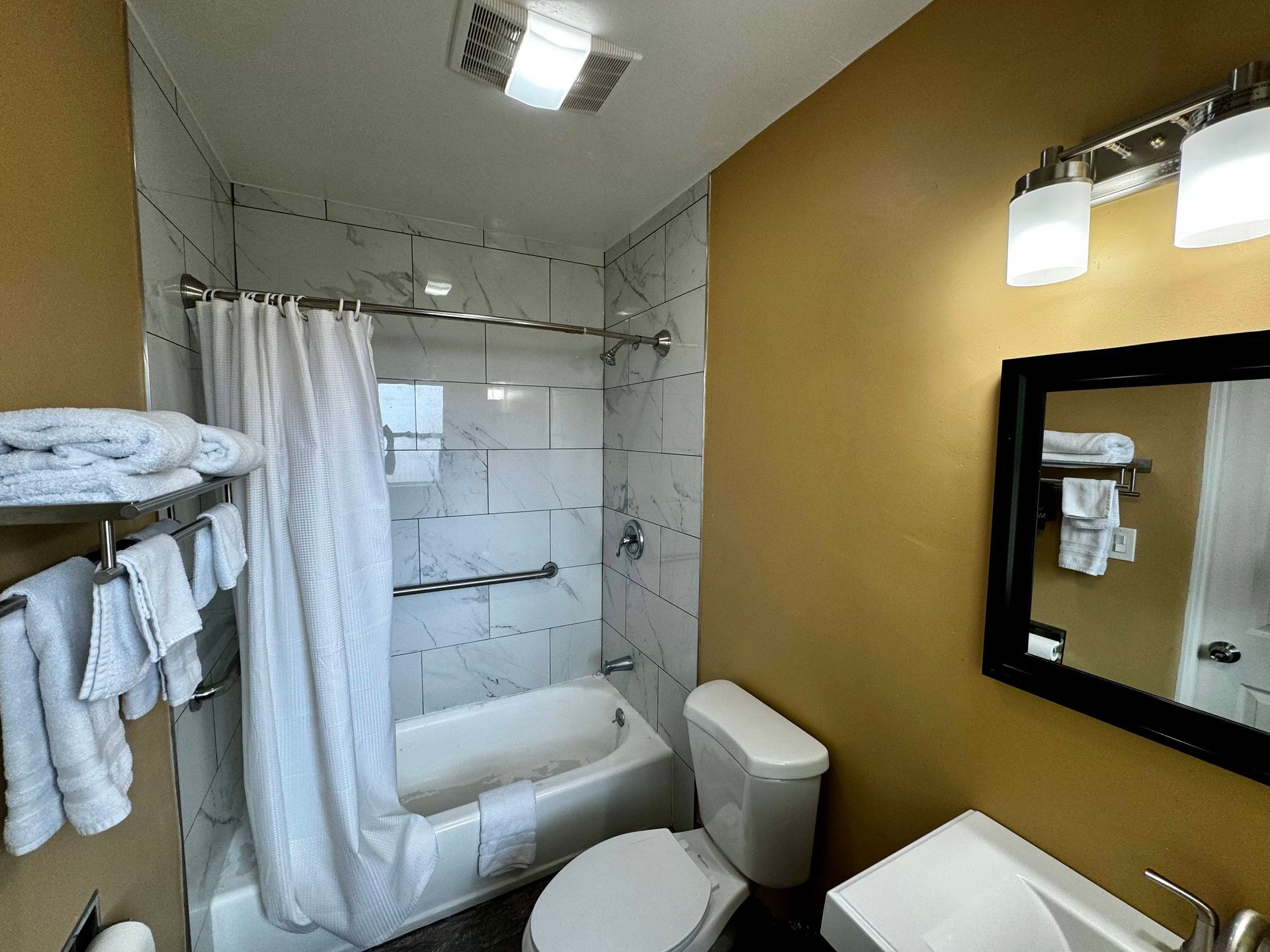 A bathroom with a white bathtub and shower curtain, a white toilet, a gold-painted wall, and a vanity mirror.