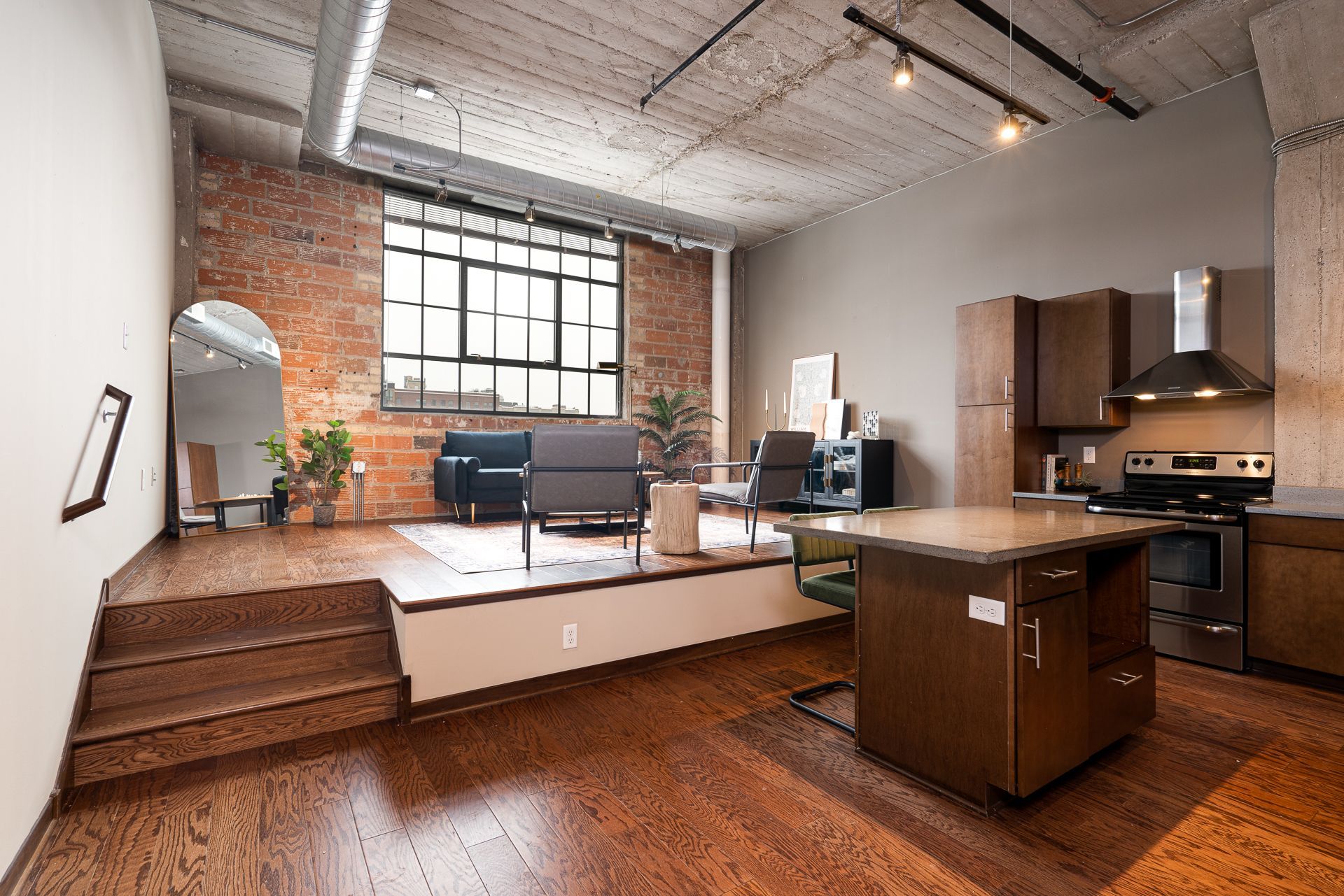 A living room and kitchen in a loft apartment with hardwood floors.