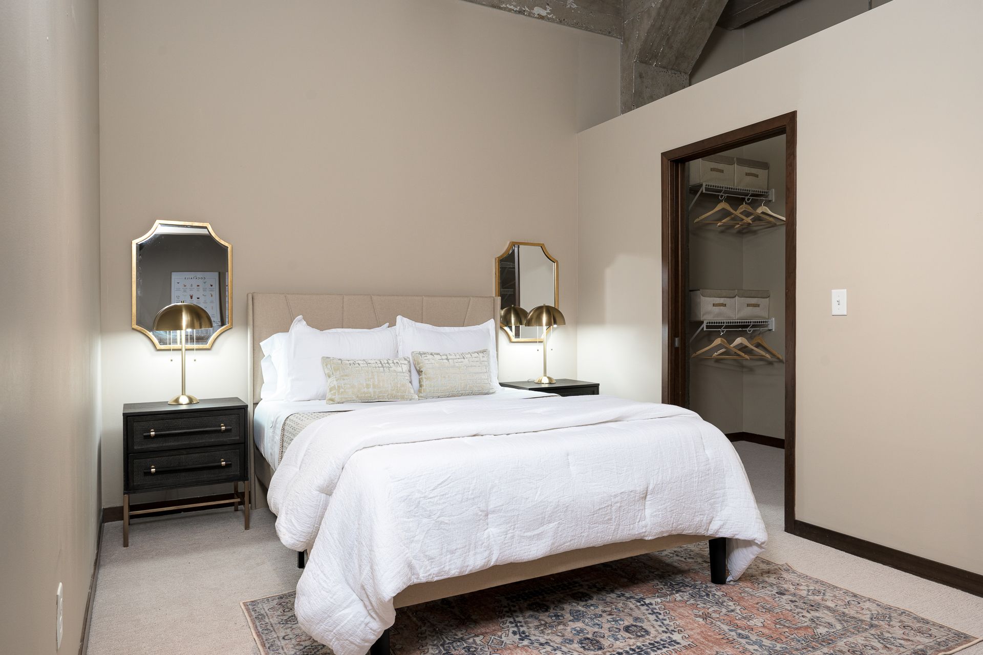 A bedroom with a bed , nightstand , lamp and mirror.