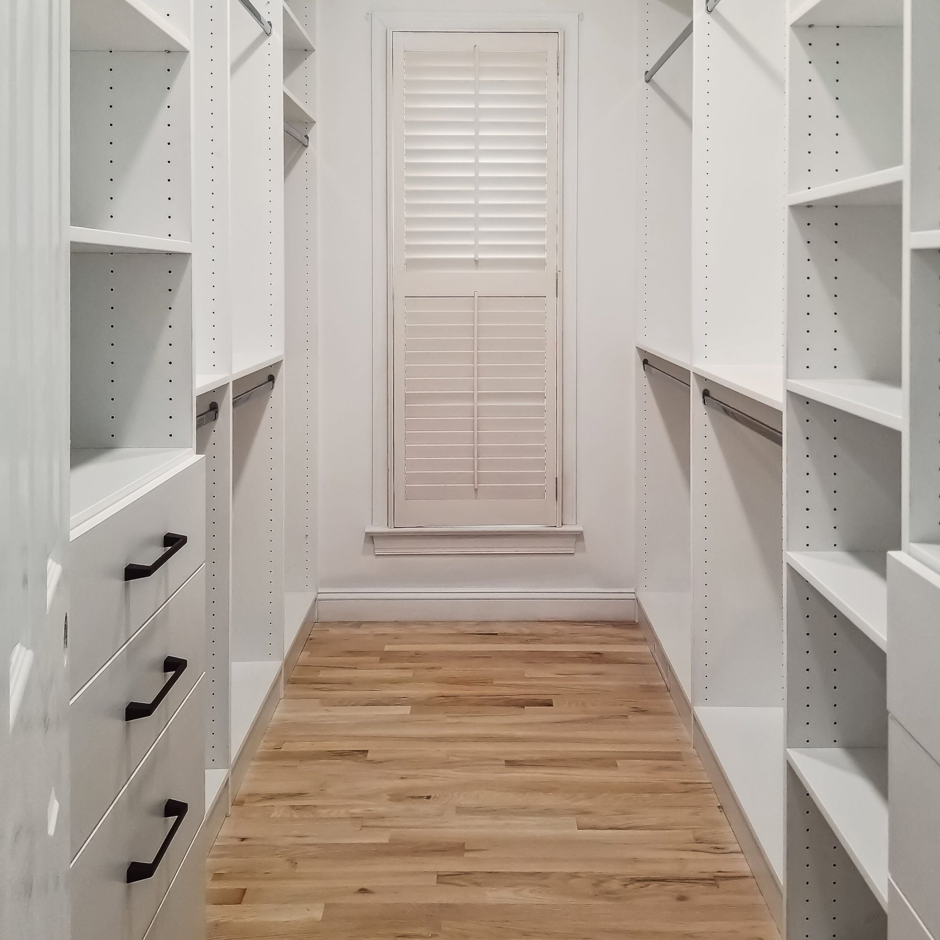 A walk in closet with wooden floors and white shelves