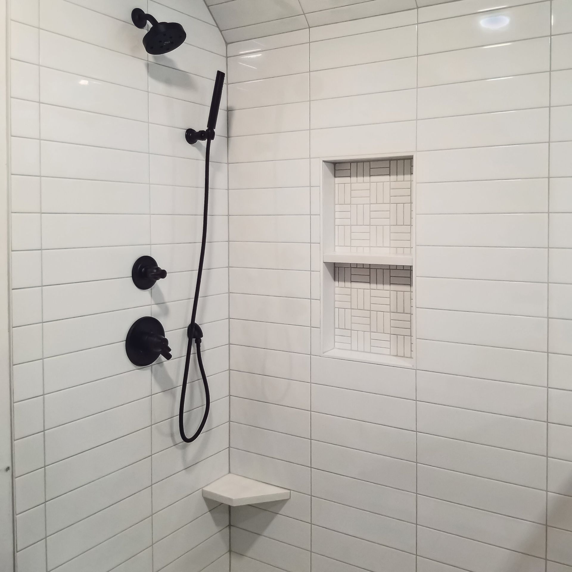A shower with white tiles and a black shower head