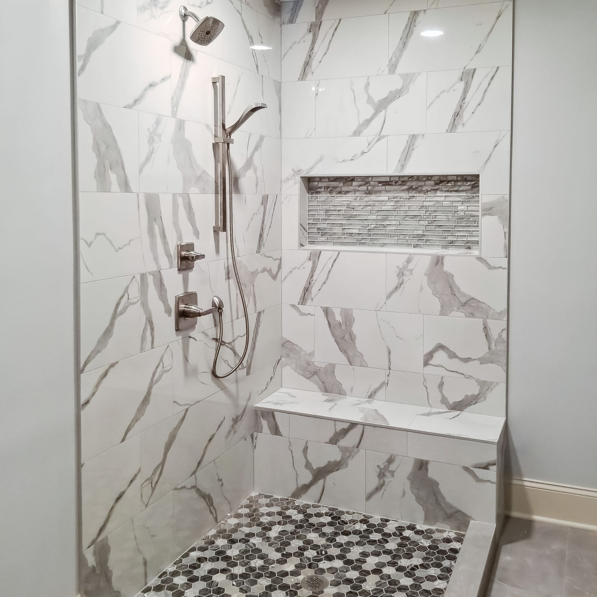 A walk in shower with marble tiles and a bench.