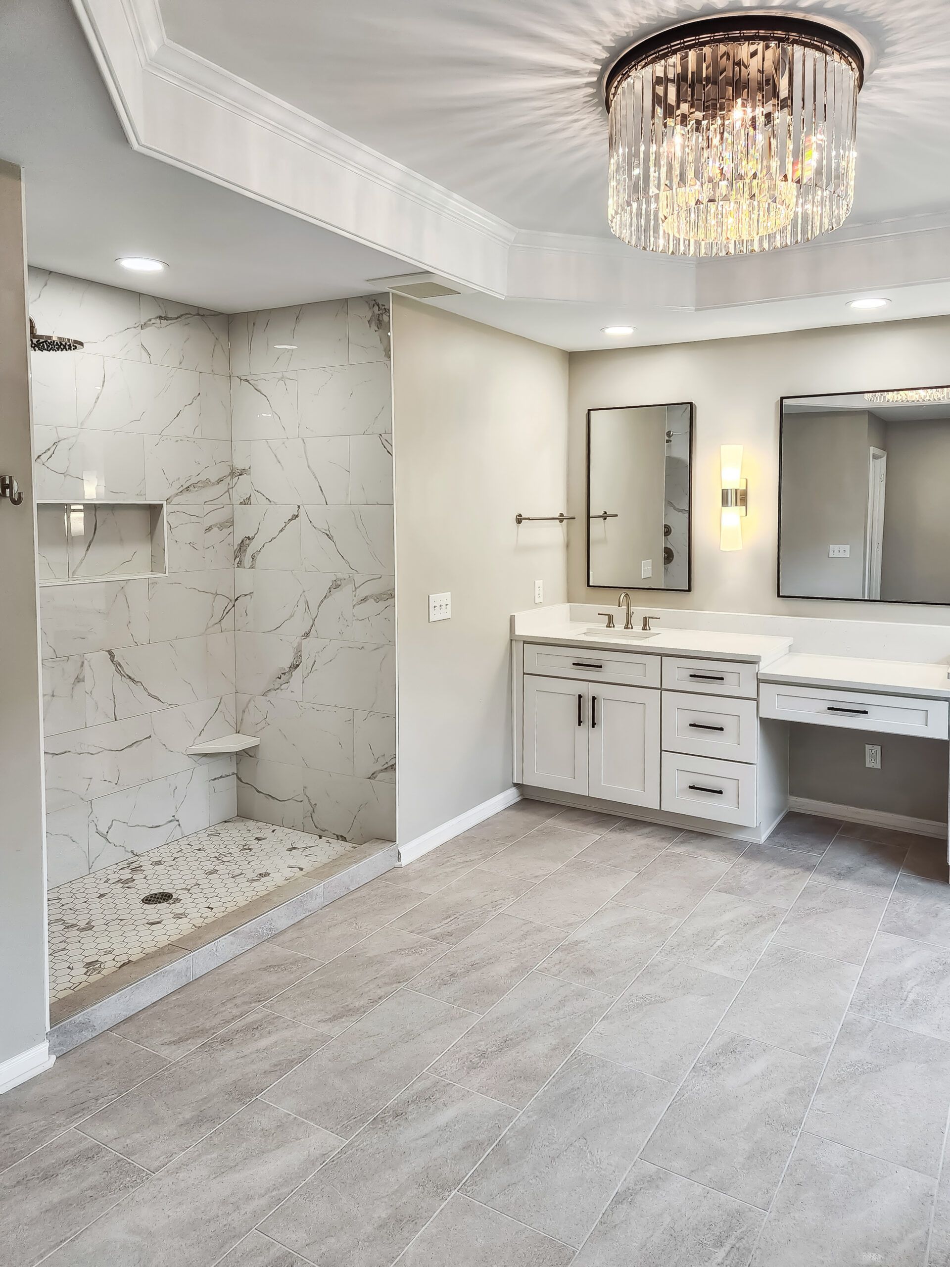 A bathroom with a walk in shower, sink, mirror and chandelier.