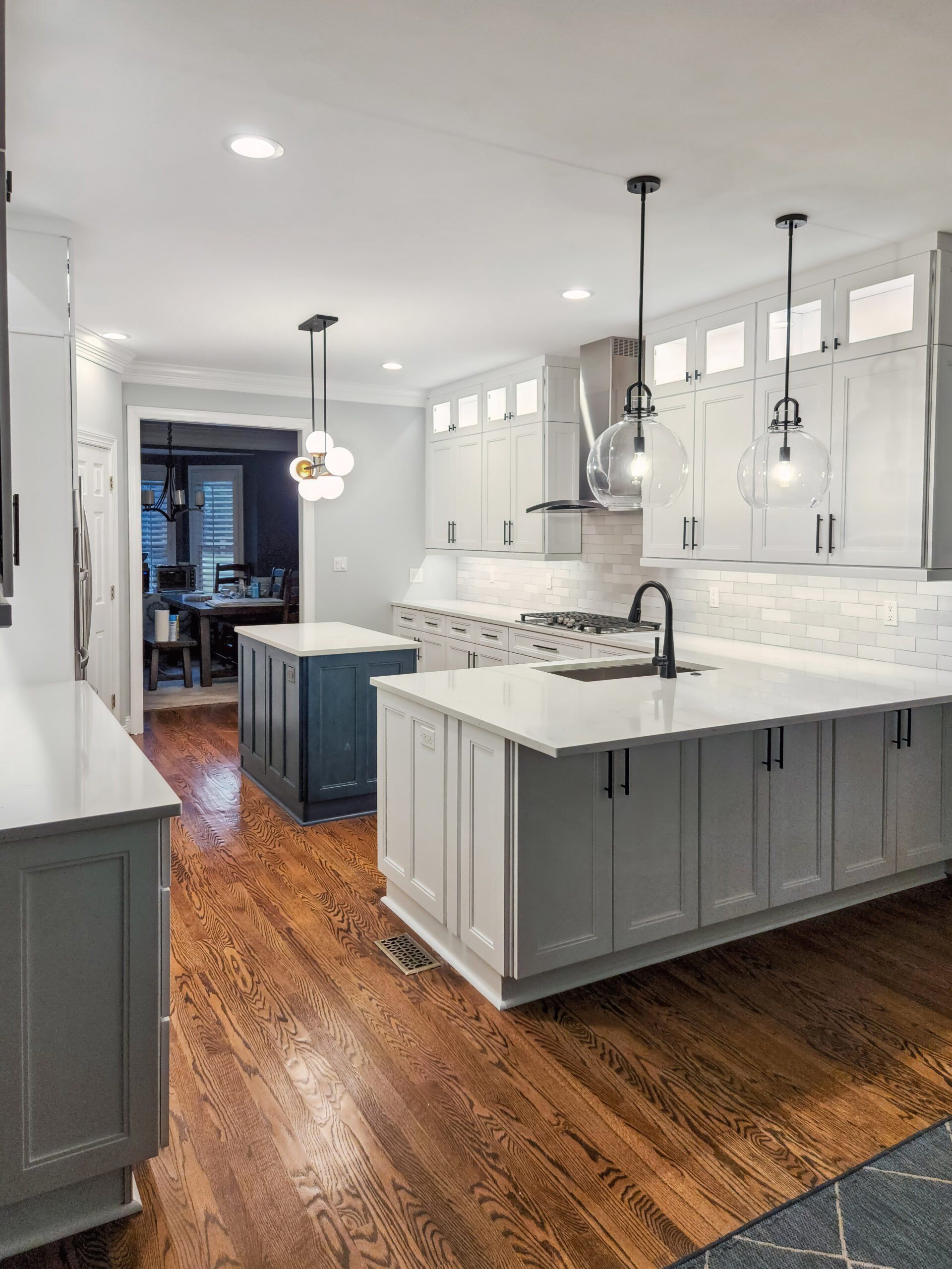 A kitchen with white cabinets and hardwood floors has a large island in the middle.