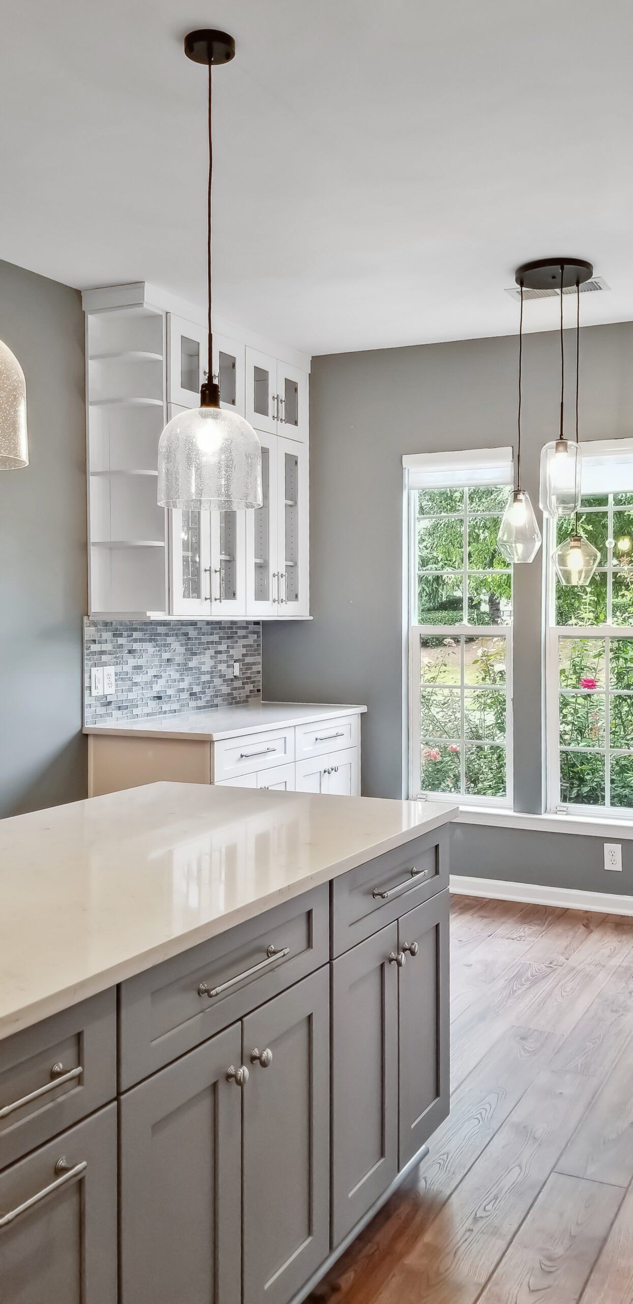 A kitchen with gray cabinets , white counter tops , and hardwood floors.