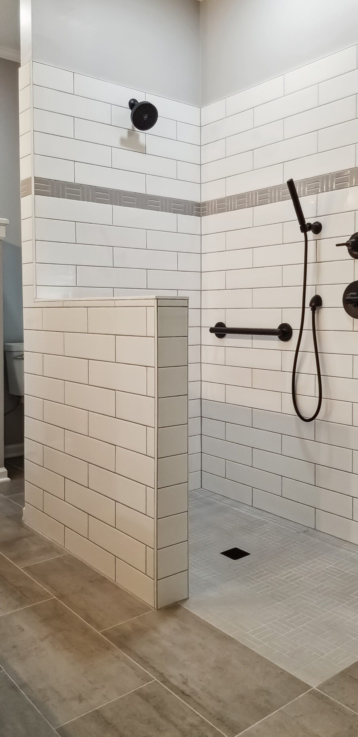 A walk in shower with a brick wall and a hand rail.