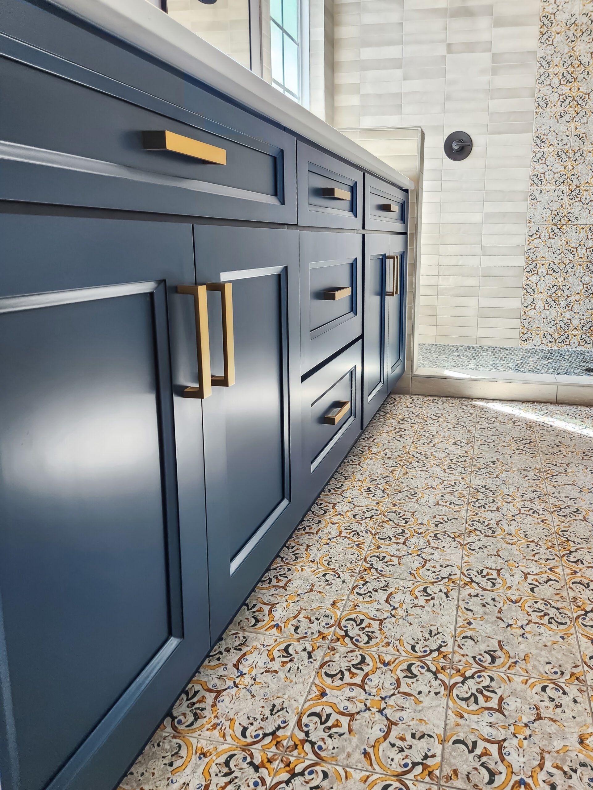 A bathroom with blue cabinets and gold handles and a tiled floor.
