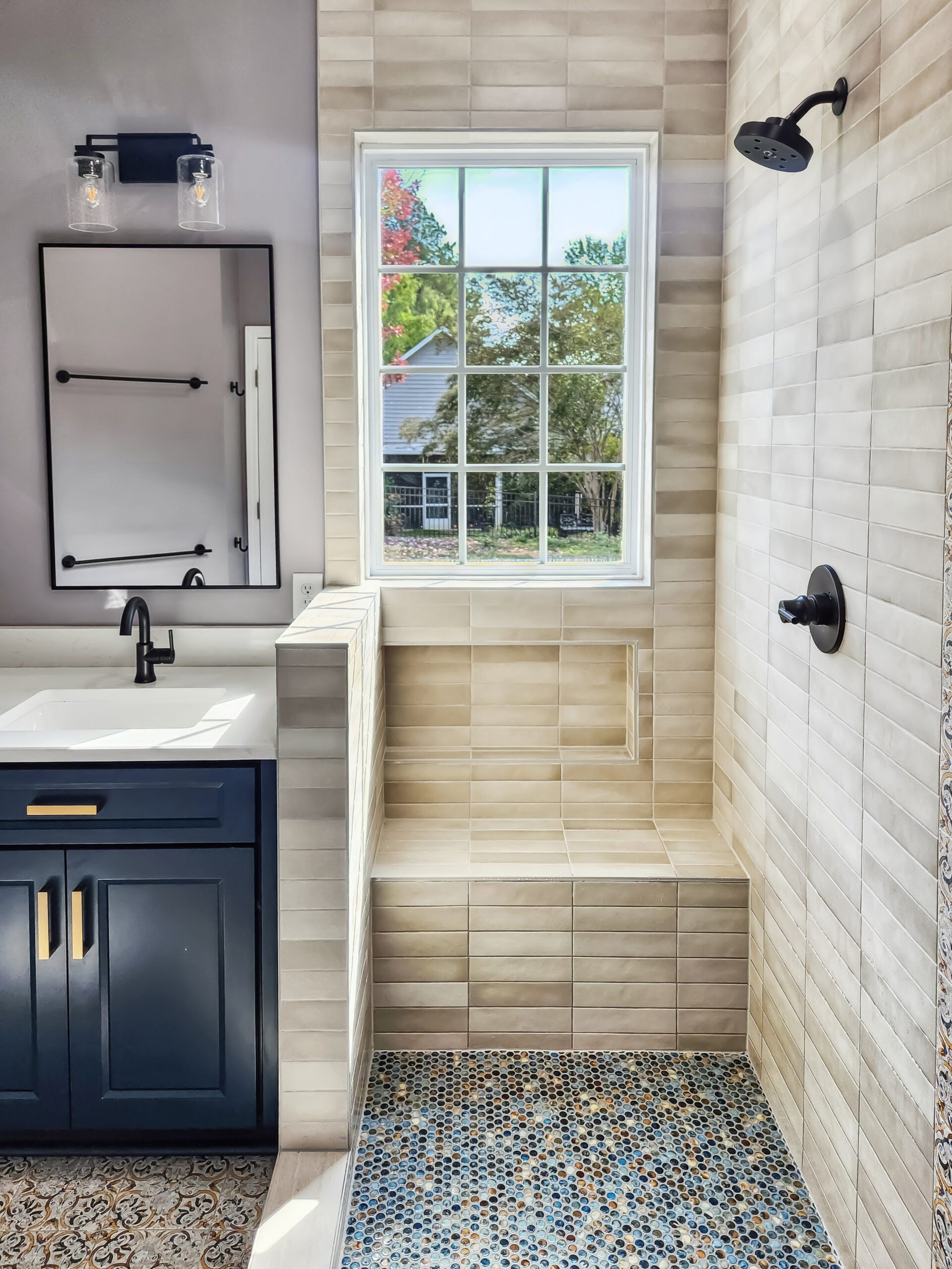 A bathroom with a sink , mirror , shower and window