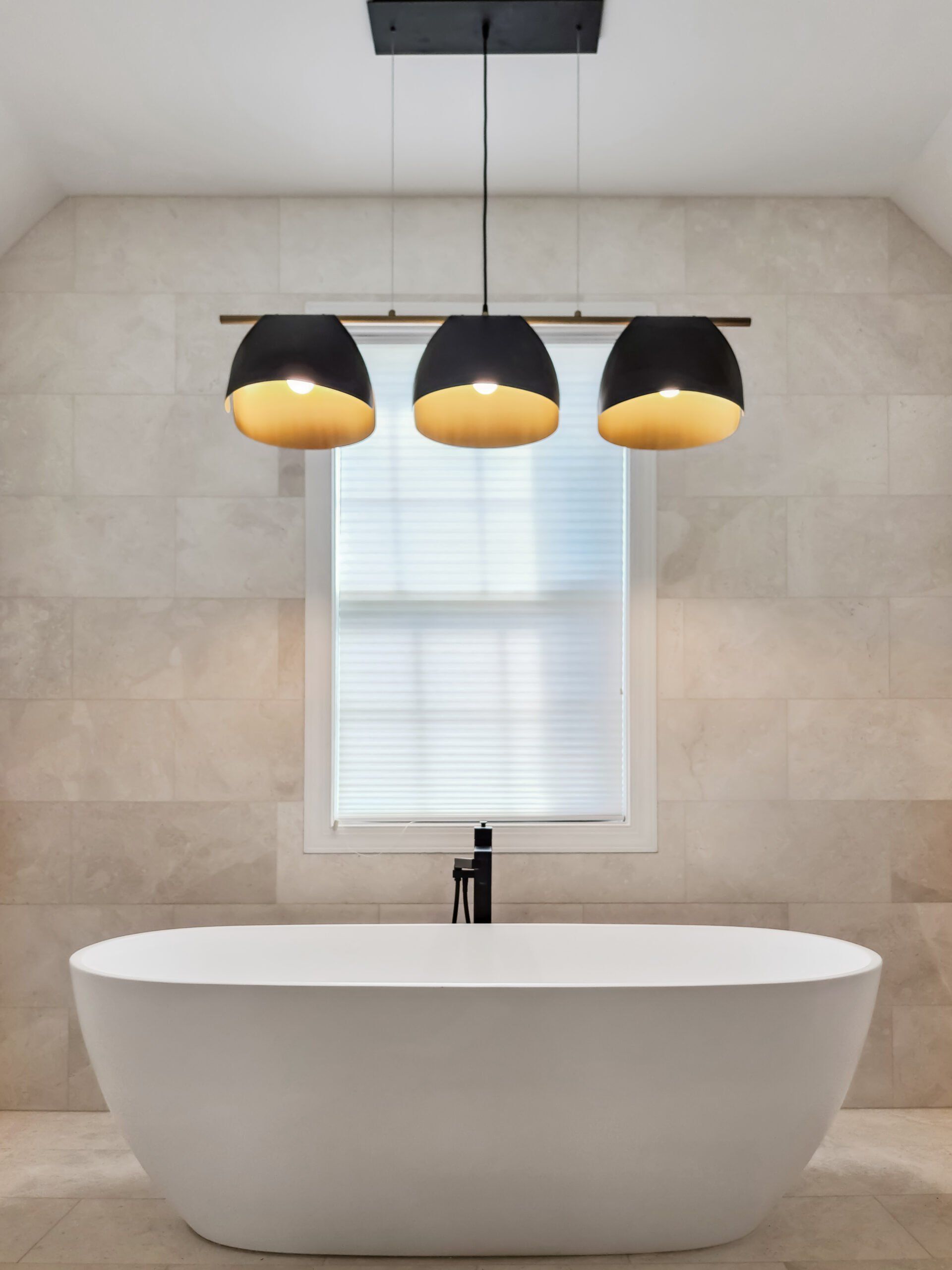 A bathroom with a bathtub and three lights hanging from the ceiling.