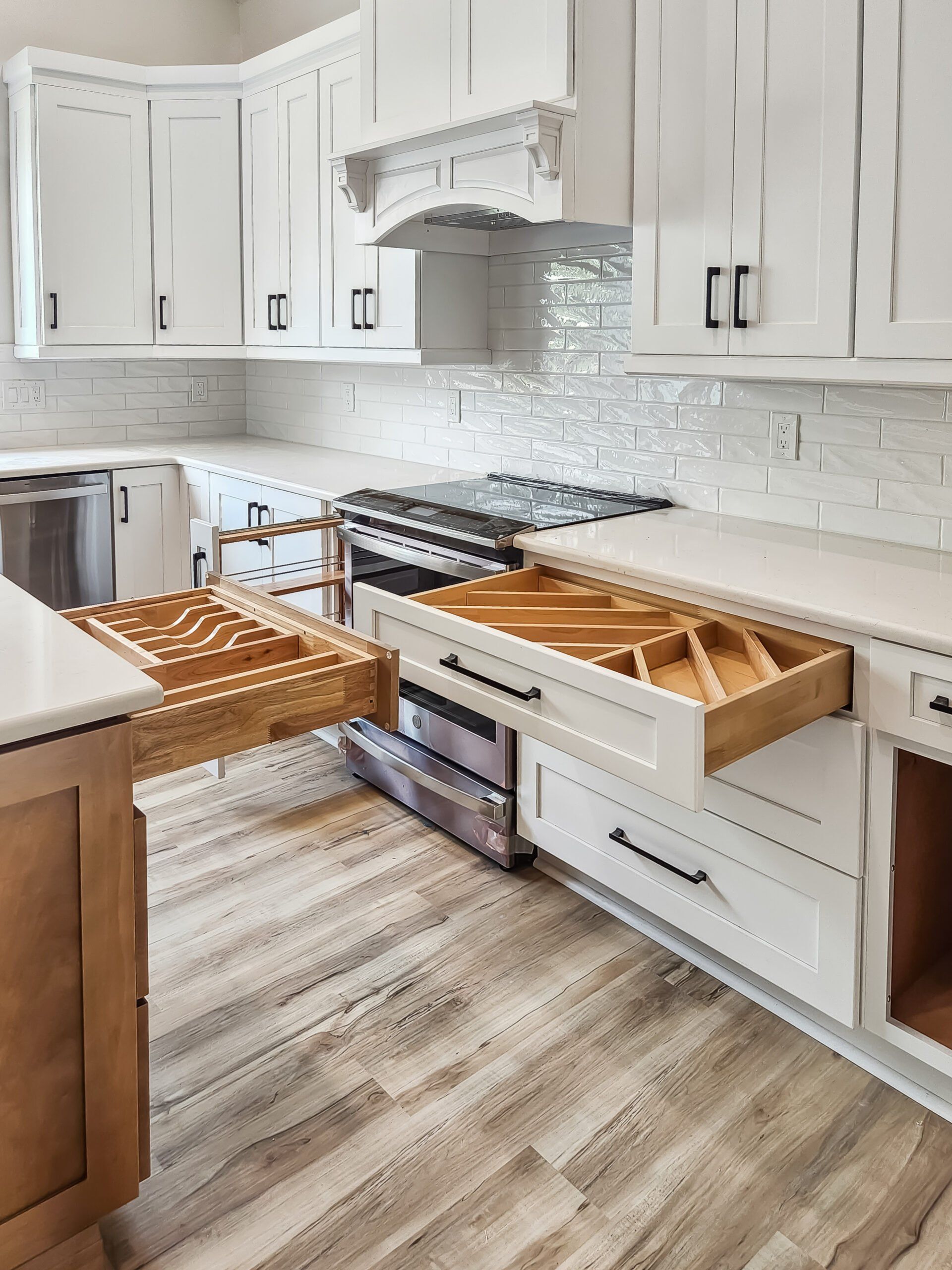 A kitchen with white cabinets and wooden floors and drawers open.