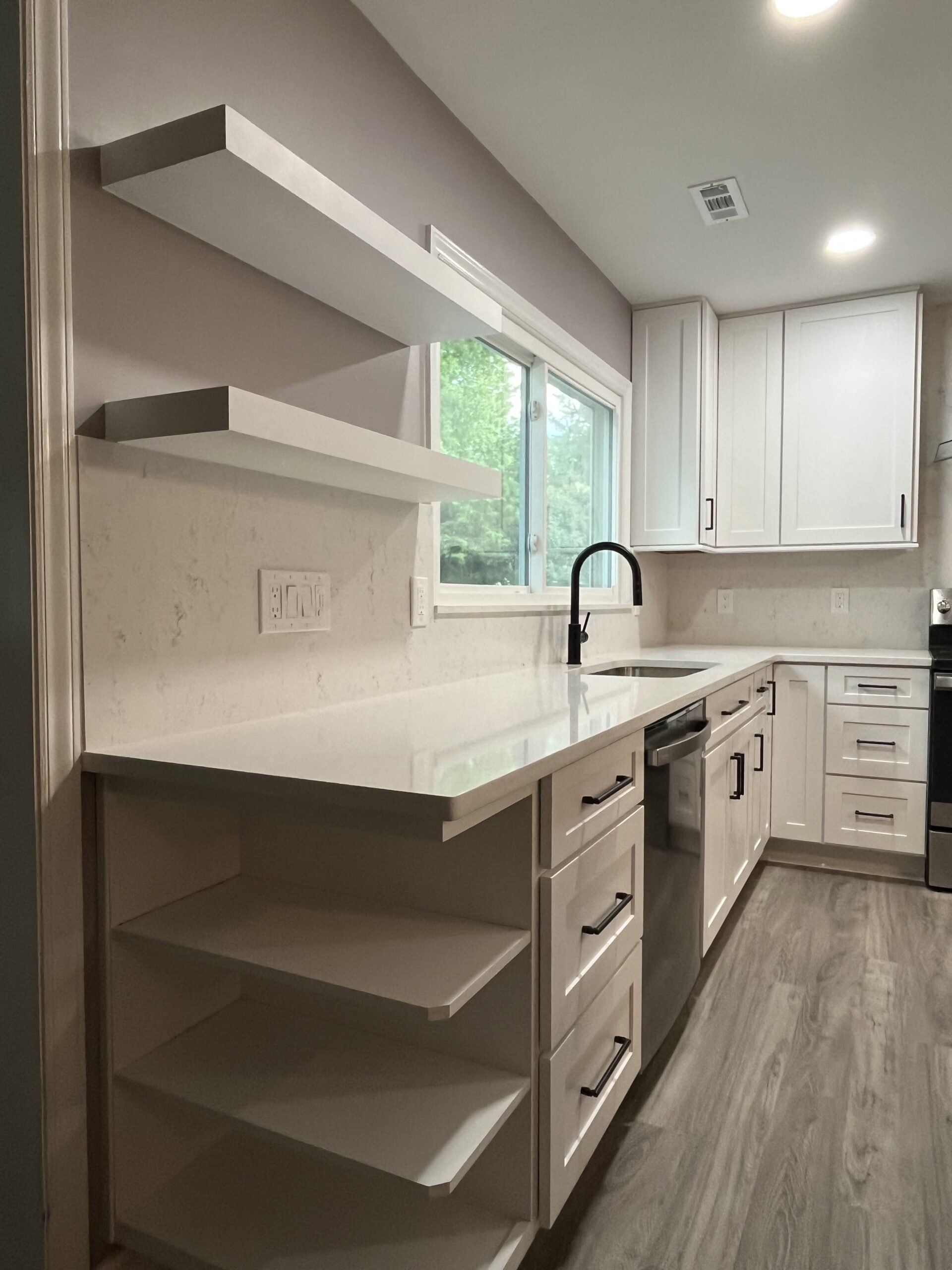 A kitchen with white cabinets , stainless steel appliances , a sink , and a window.