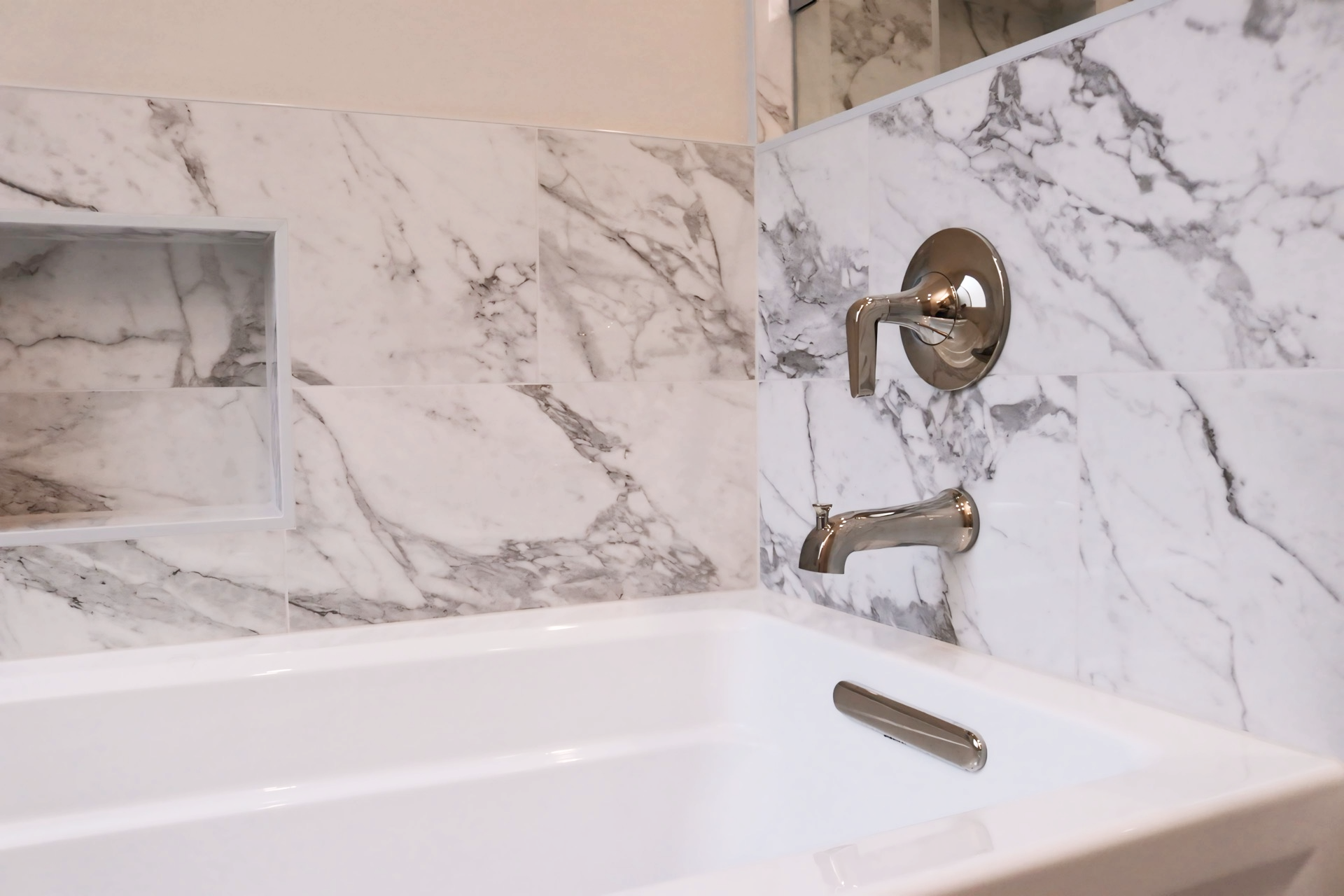 A bathtub in a bathroom with a marble wall behind it.