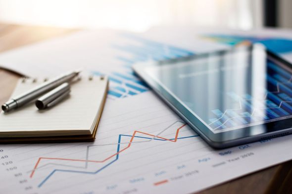 Tablet, notepad, pen, and graphs on a wooden surface, suggesting financial analysis.