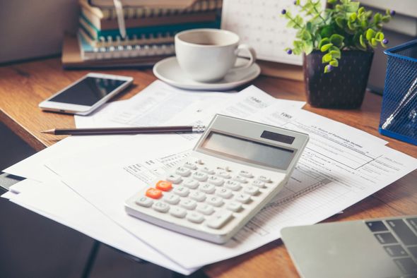 Desk with calculator, paperwork, coffee, phone, pen, and laptop; office setting.
