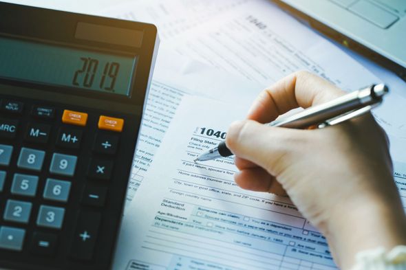 Hand filling out a tax form with a pen, calculator displaying 