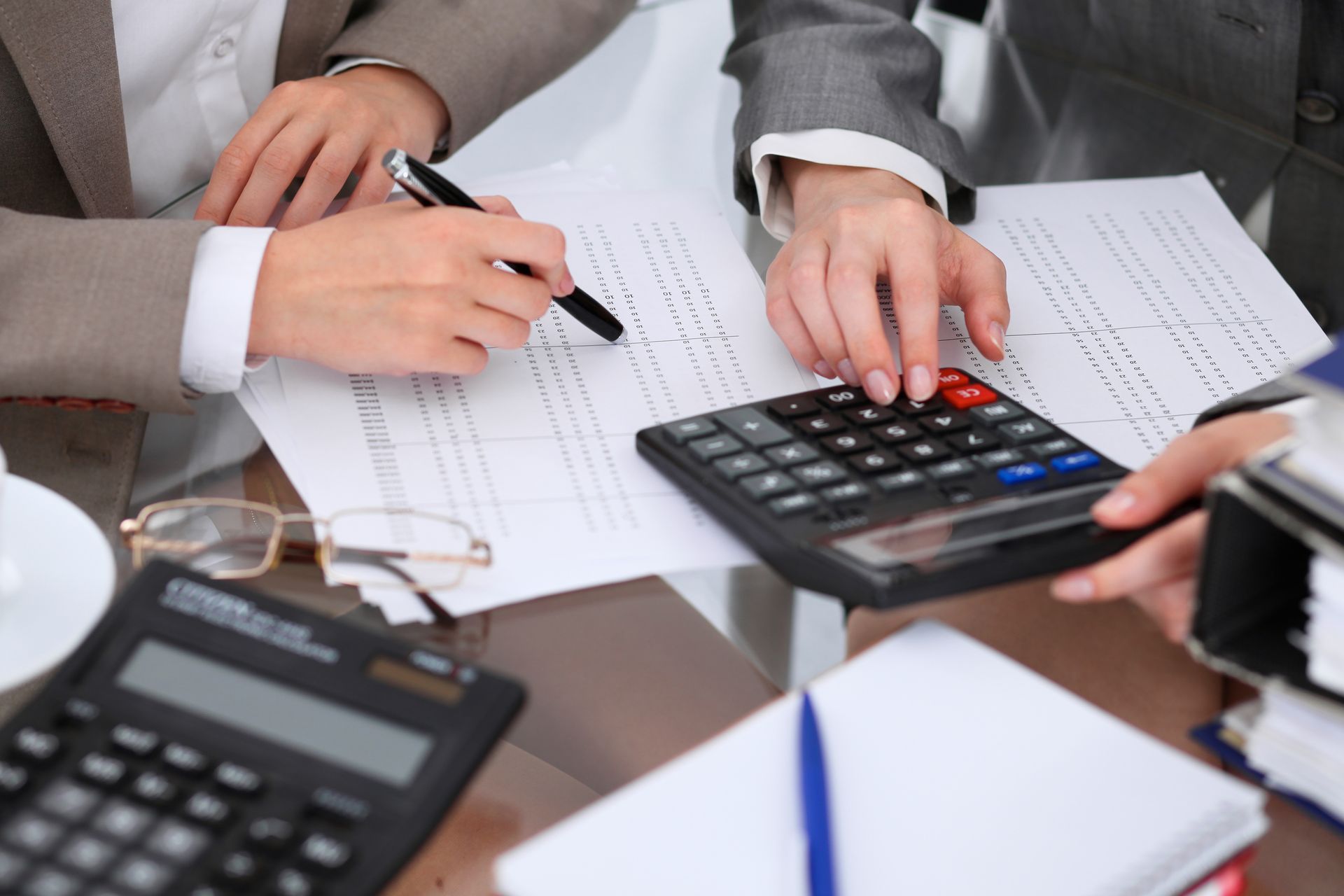 Hands using calculator and pen on paperwork; office setting.