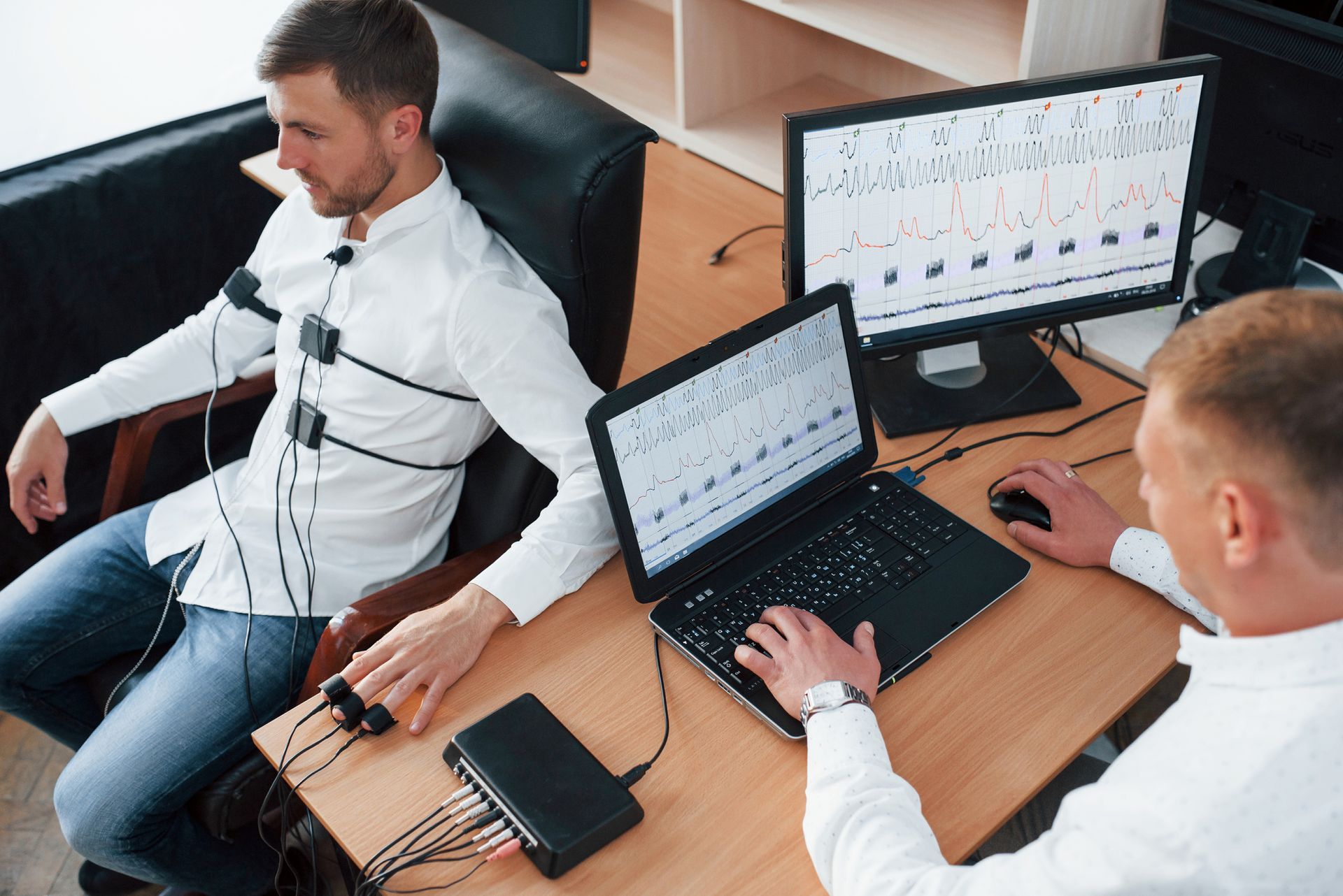 Two men are at a desk with laptops and monitors, collaborating on private investigation projects.