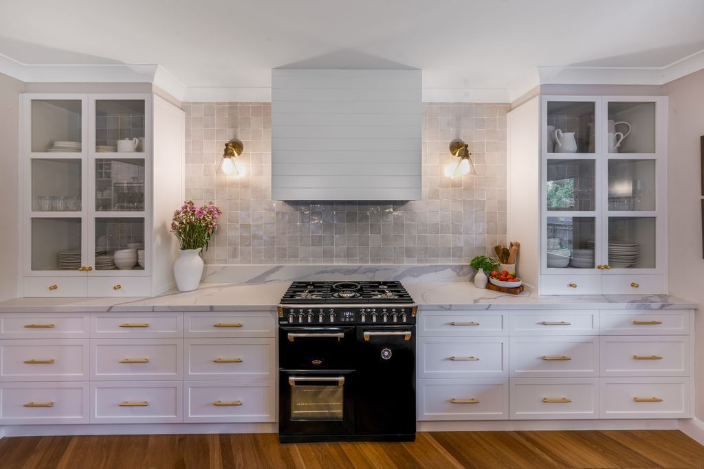 Modern white kitchen with black stove, tile backsplash, gold accents, and wooden floor