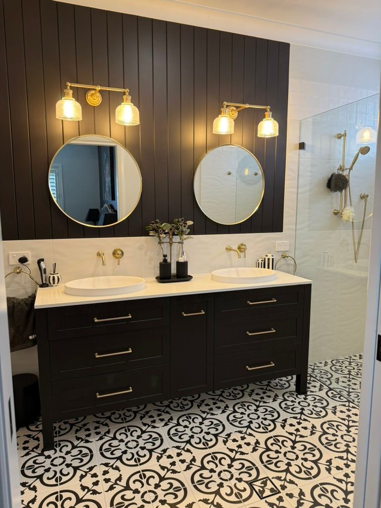 Elegant bathroom with double black vanity, round mirrors, warm sconces, and patterned black-and-white tile floor
