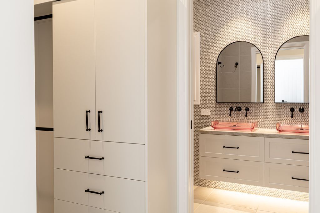 Modern bathroom vanity with arched mirror, white cabinets, and pink countertop lighting