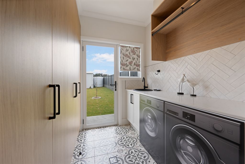 Bright laundry room with washer, dryer, wood cabinets, and a door to a grassy backyard.