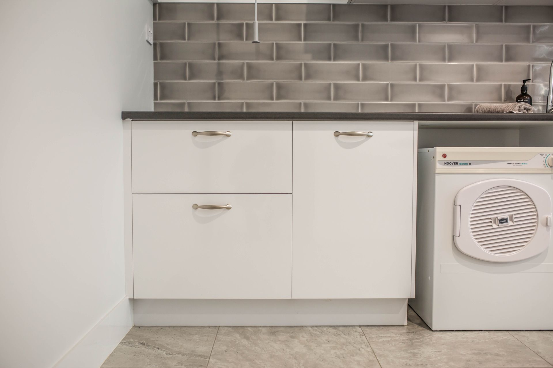 Modern Laundry Nook with White Cabinets, Gray Tile Backsplash, and A Stacked Washer — Simmonds Kitchens in Walcha, NSW