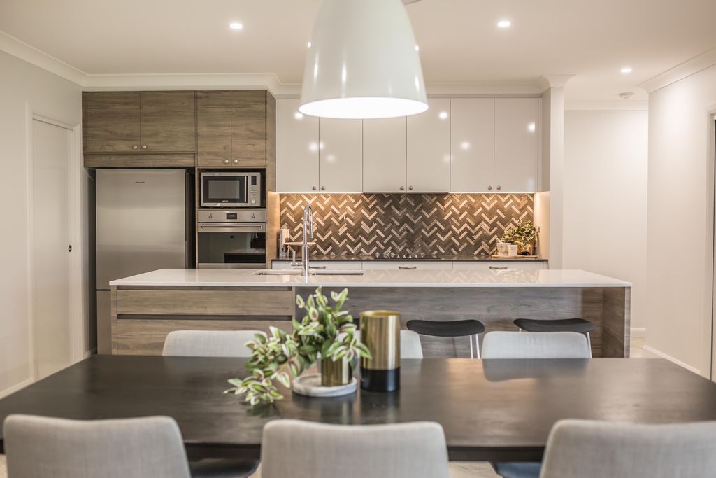 Modern kitchen with island, pendant light, white cabinets, and herringbone backsplash; dining table in foreground