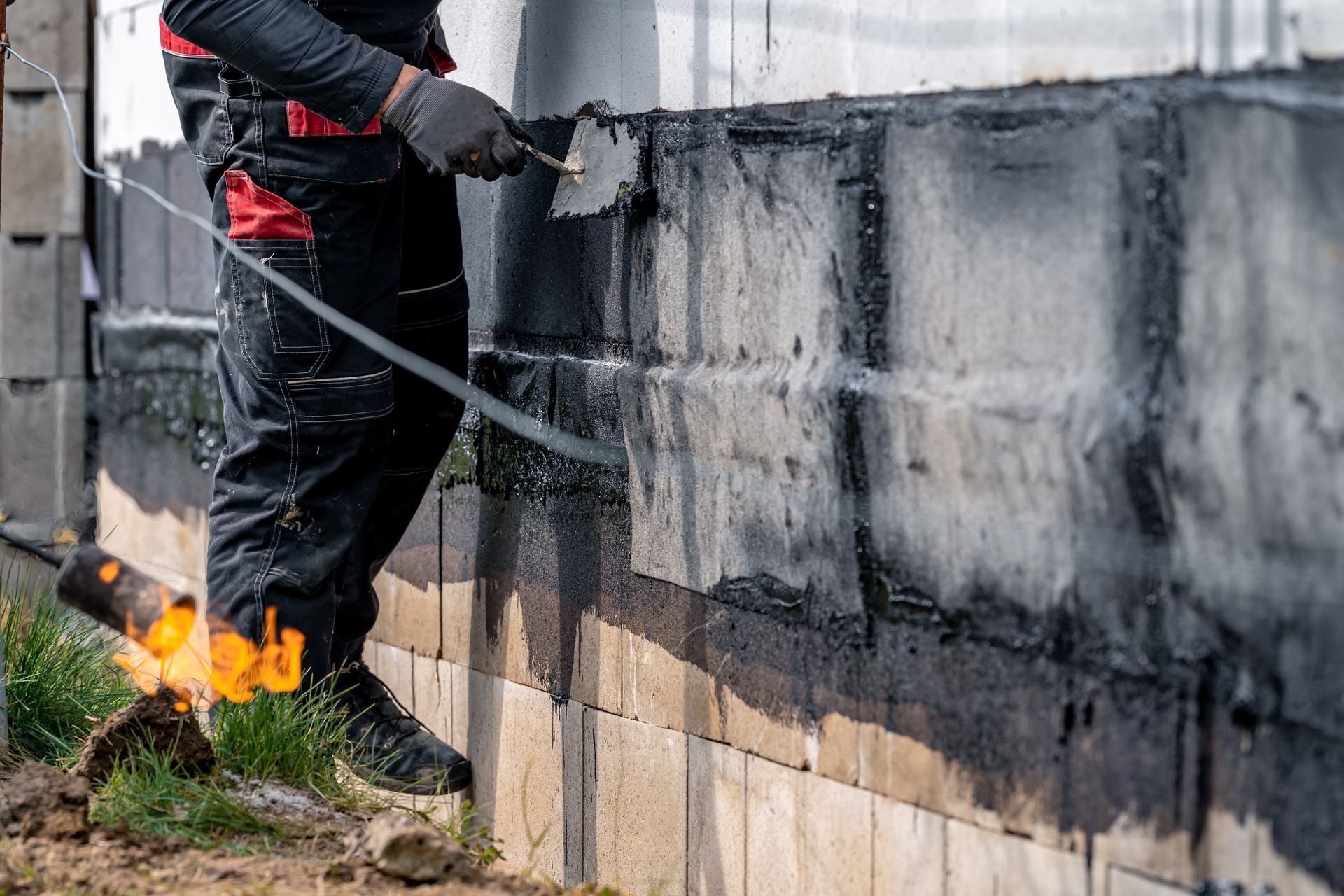 a man in black overalls and safety gear painting a brick wall