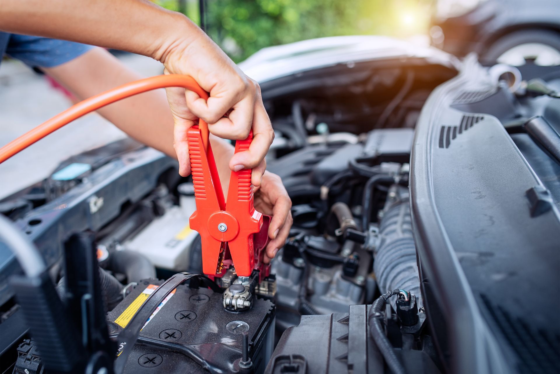 Person using jumper cables to connect to a car battery.