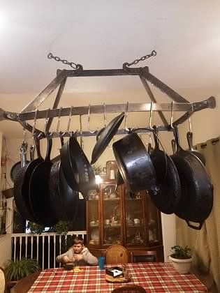 A man is sitting at a table in a kitchen with pots and pans hanging from the ceiling.
