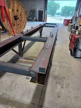 A large metal structure is sitting in a garage next to a wooden spool.