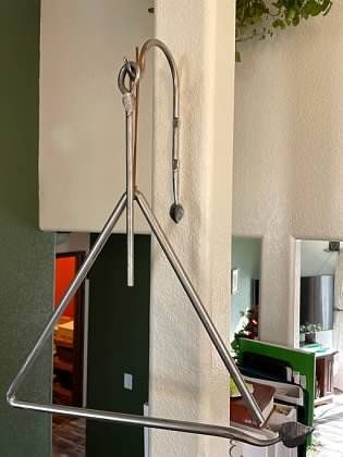 A metal triangle is hanging from a pole in a room.