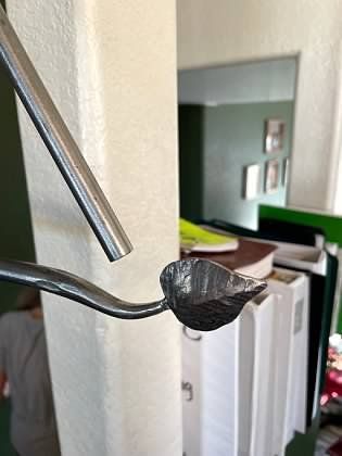 A metal spoon with a leaf on it is hanging on a wall.