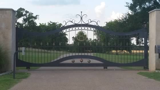 A black wrought iron gate is open to a driveway.