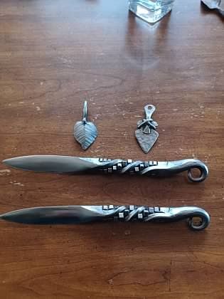 Two knives and two pendants are sitting on a wooden table.