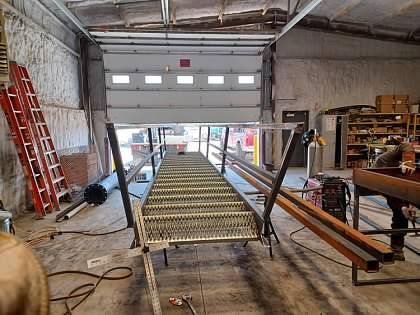 A metal staircase is being built in a garage with a garage door open.