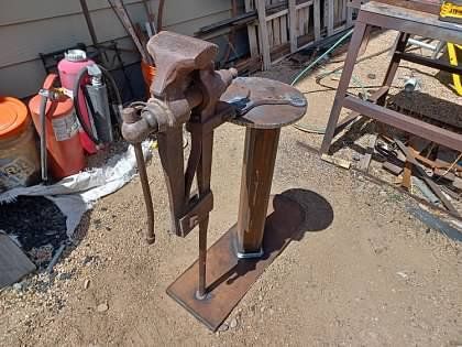 A vise is sitting on top of a wooden stand on the ground.