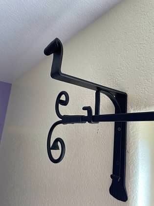 A black metal bracket is hanging on a white wall.