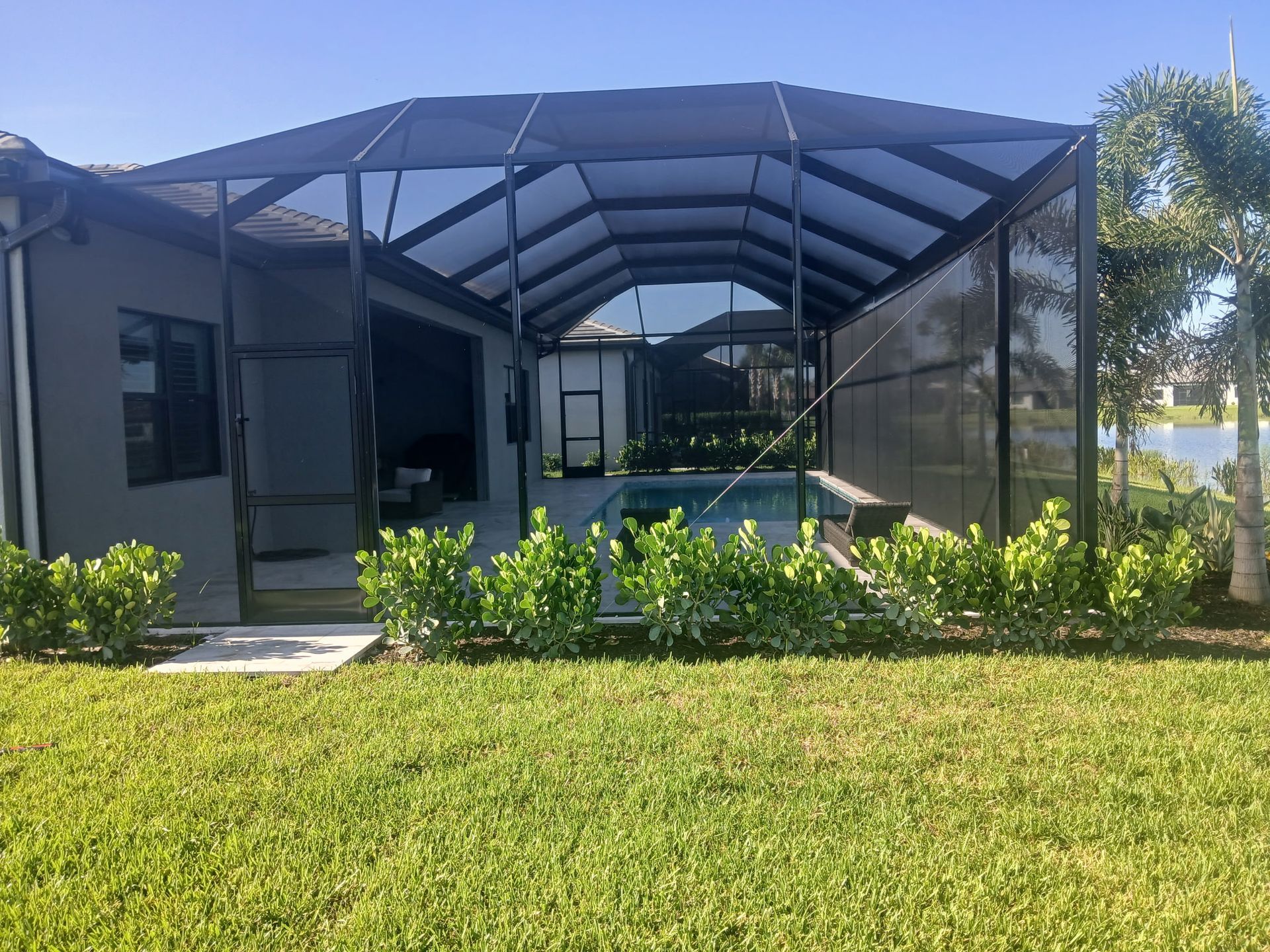 Person working on a screened pool enclosure near a pool. Sunny day. Black metal frame.