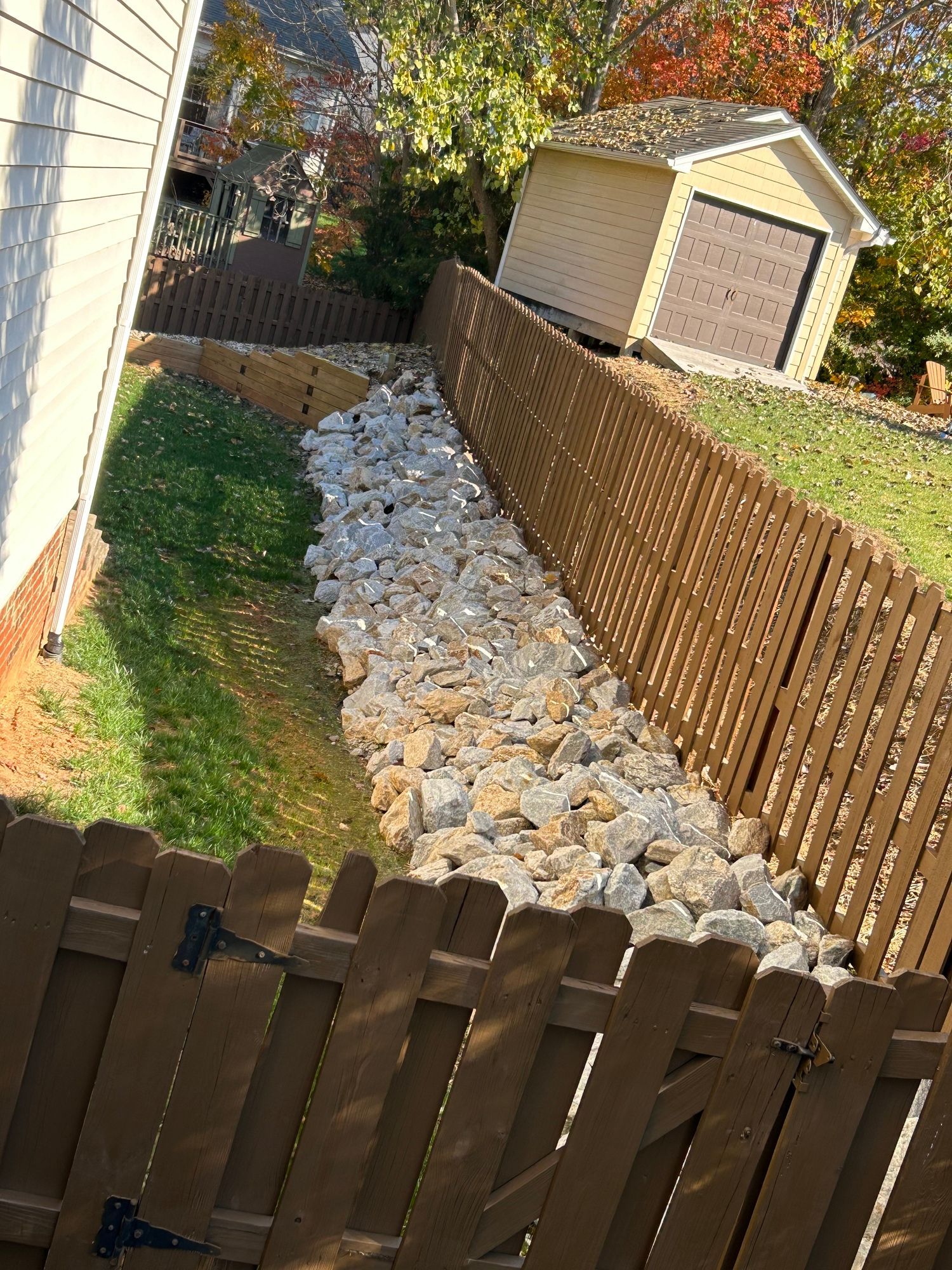 A wooden fence surrounds a rocky area in front of a house.