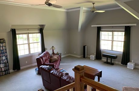 Spacious living room with high ceiling. Red leather sofa, windows with dark curtains, and audio speakers.