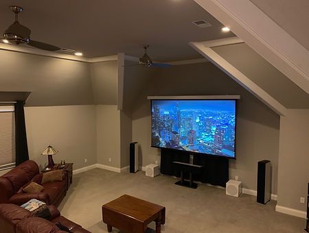 Home theater with large screen, speakers, and leather sofa in a room with a sloped ceiling.