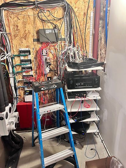 Electrical wiring and equipment on a wooden wall in a basement, with a ladder and shelves.