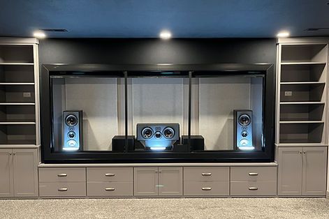 Built-in entertainment center with speakers, shelves, drawers, and a black recessed area on a gray wall.