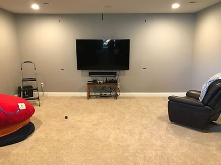 Living room with mounted TV, soundbar, and furniture against a gray wall, on a beige carpet.