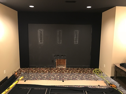 Basement wall under construction: black accent wall, beige walls, wood flooring in progress, and exposed framing.