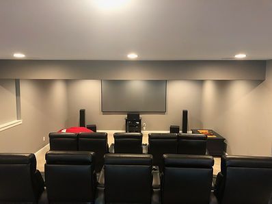 Home theater with black leather recliners, screen, speakers, and media cabinet on gray walls.