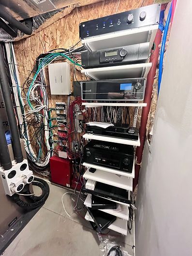 Audio-visual equipment stacked on shelves in a utility room. Wiring and pipes visible.