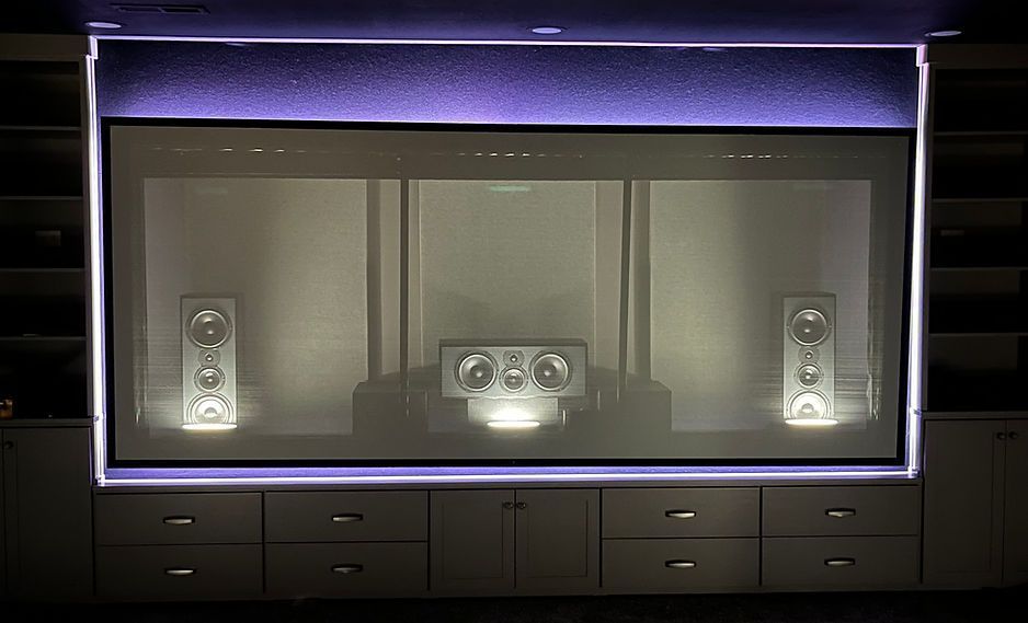 Home theater setup with screen, speakers, and cabinet. Purple lighting accents the top and bottom.